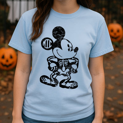 Person wearing a light blue t-shirt with a skeleton Mickey Mouse design, surrounded by pumpkins.