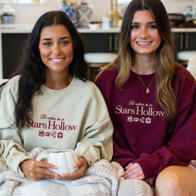 Two women wearing 'I'd rather be in Stars Hollow' sweatshirts sitting together.